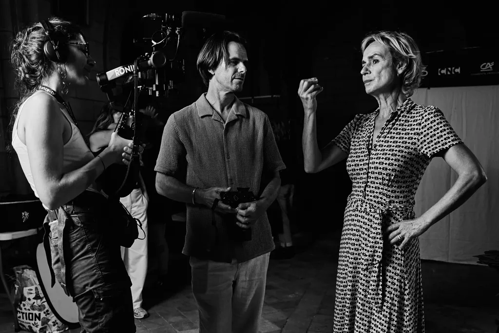 A camerawoman in headphones films a man and a woman in a printed dress with a stabilised camera, black and white.