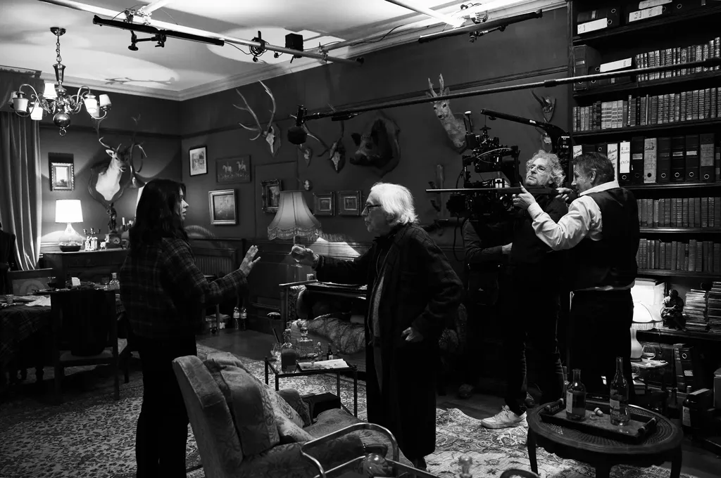 A crew filming in a library hung with hunting trophies, camera on an arm and a boom above the actors, black and white.