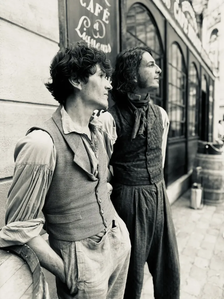 Two young men in waistcoats in front of a café front, looking off to the right, black and white.