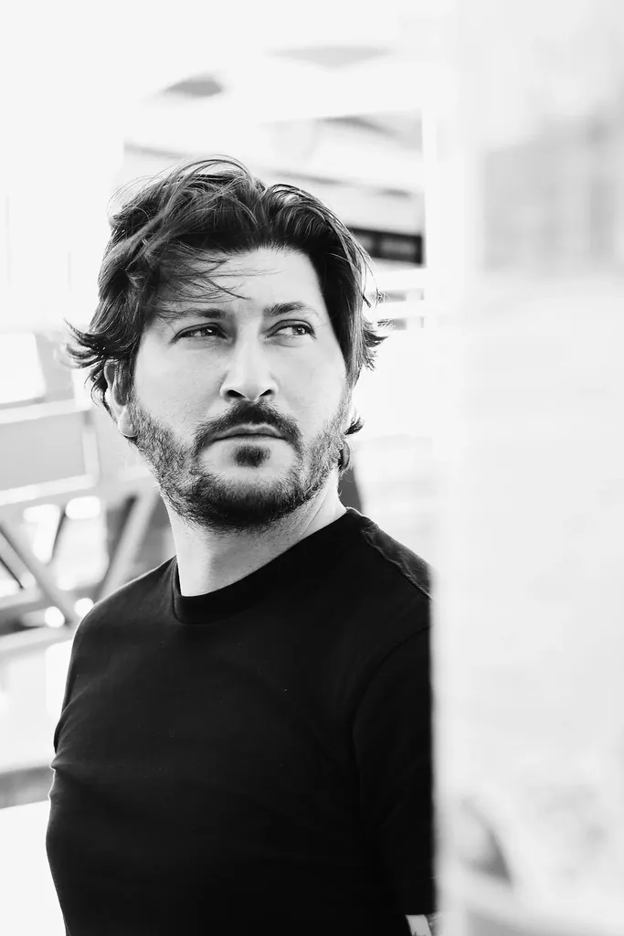 A bearded man in a black t-shirt looking aside in soft white light, in black and white.