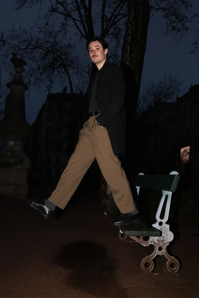A young man in beige trousers jumping beside a bench at night in a public garden.