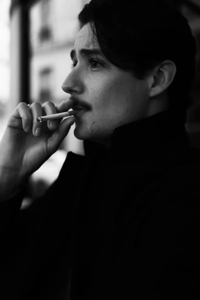 Profile of a young man with a moustache, a cigarette at his lips, high contrast, in black and white.