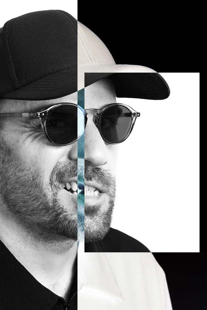 Black and white portrait of a bearded man in a cap and sunglasses, cut vertically into two offset halves, one on a black ground, the other in front of a white rectangle, with a thin bluish strip in the middle.