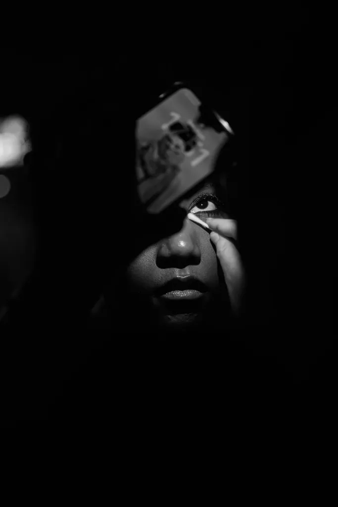 Black and white, backstage: a face in shadow, one eye lit, while a hand applies make-up.