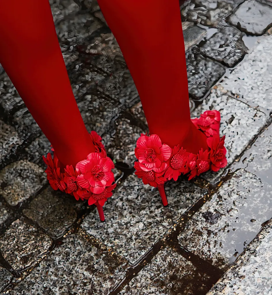 Colour, close-up on wet cobblestones: red tights and pumps covered with red flowers.