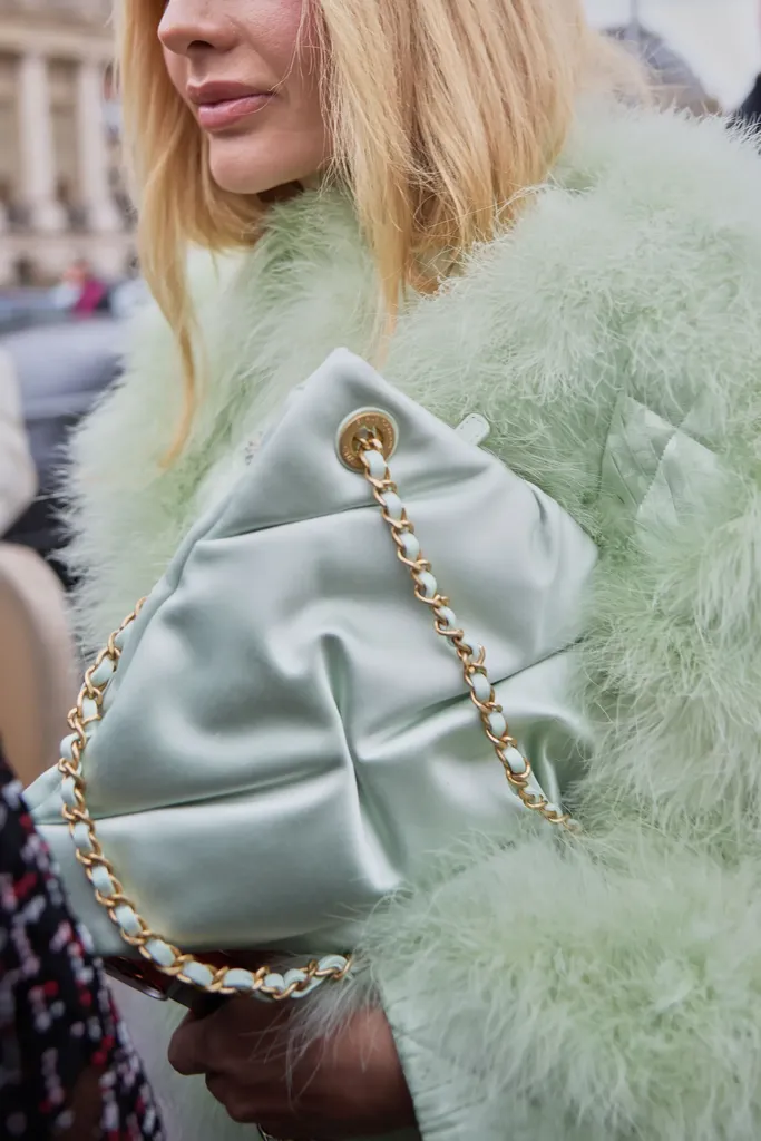 Colour, close-up: a mint quilted bag with a gold chain held against a feather coat of the same colour.