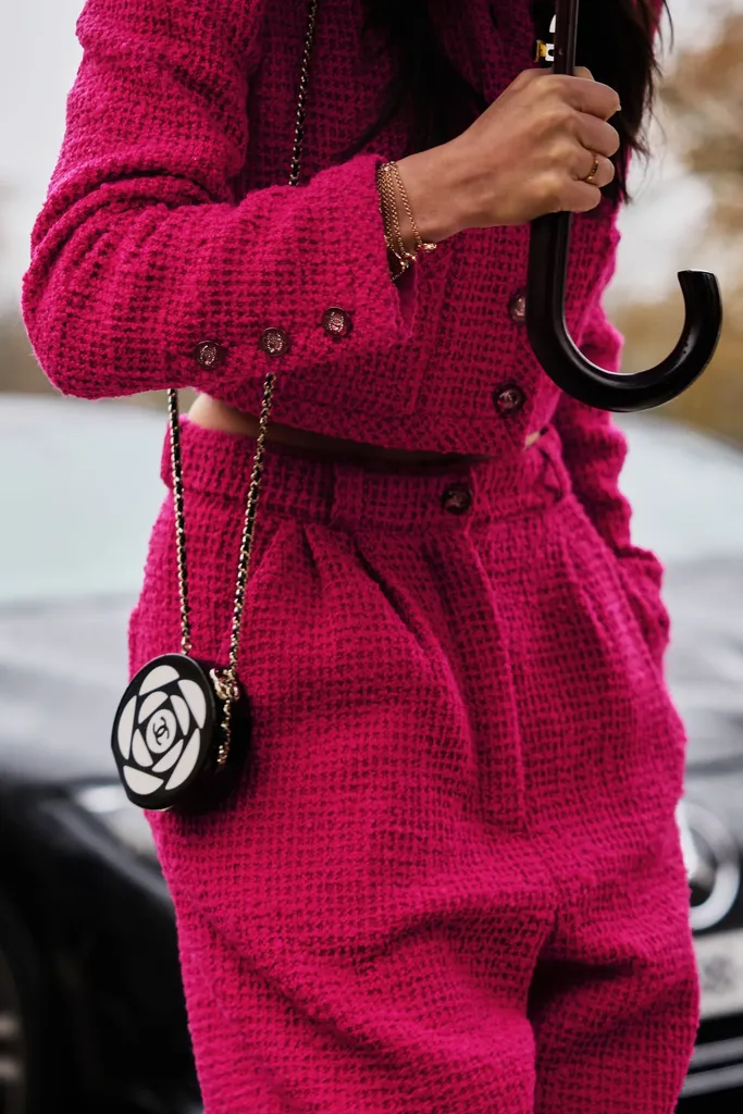 Colour, close-up: a fuchsia tweed suit, a small round black and white bag and an umbrella with a curved handle.