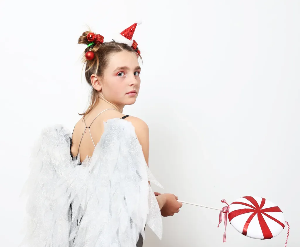 Girl seen from behind with white wings, holding a red and white striped lollipop, looking over her shoulder, white ground.