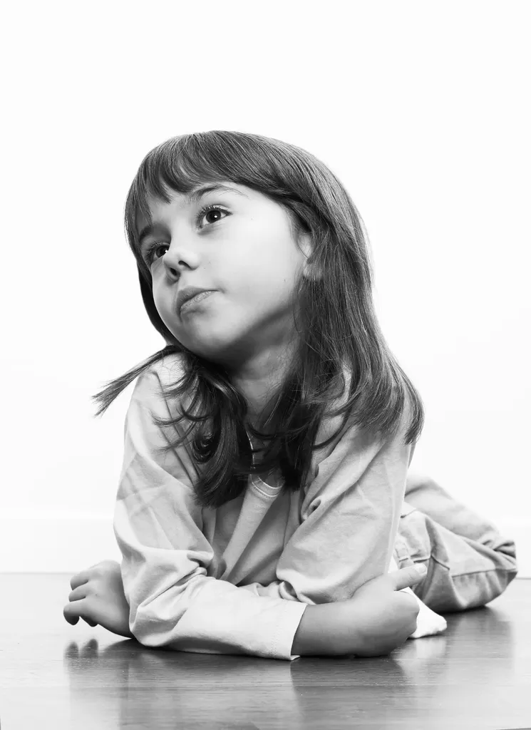 Girl lying on a wooden floor, propped on her elbows, looking up, in black and white.