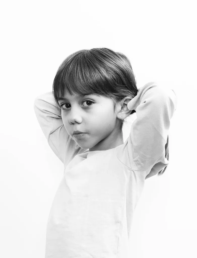 Boy with his hands behind his head, light T-shirt, on a white ground, in black and white.