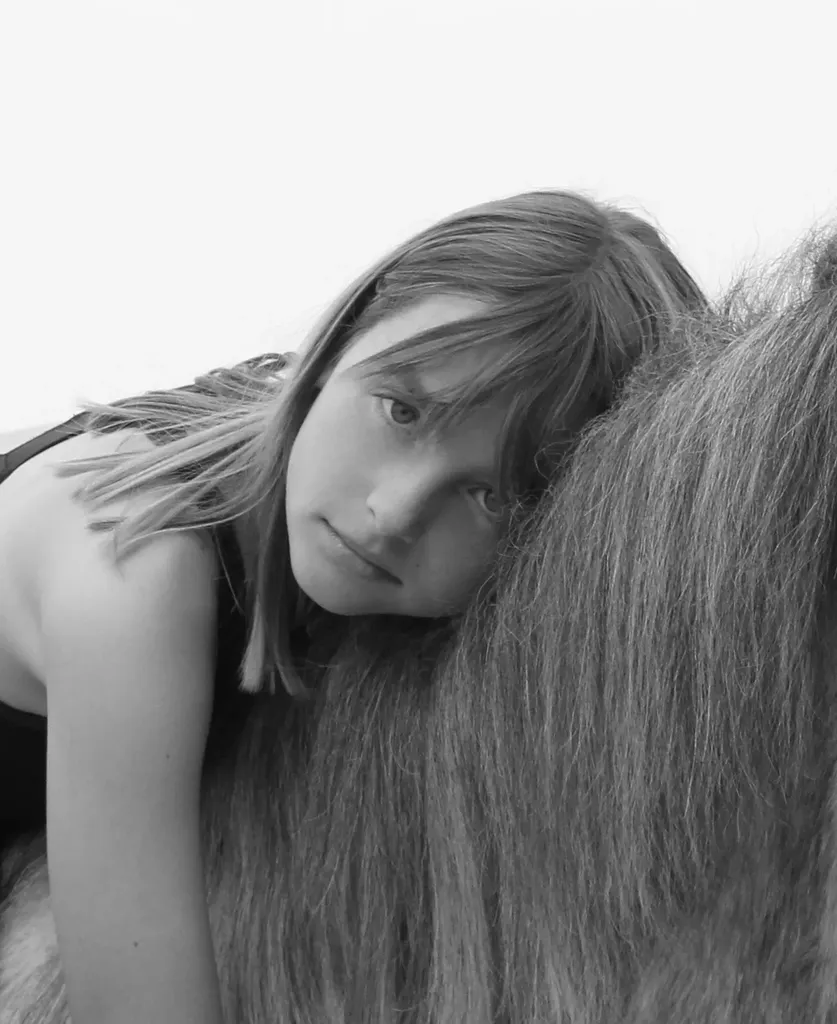 Girl resting her cheek against a horse’s mane, in black and white.