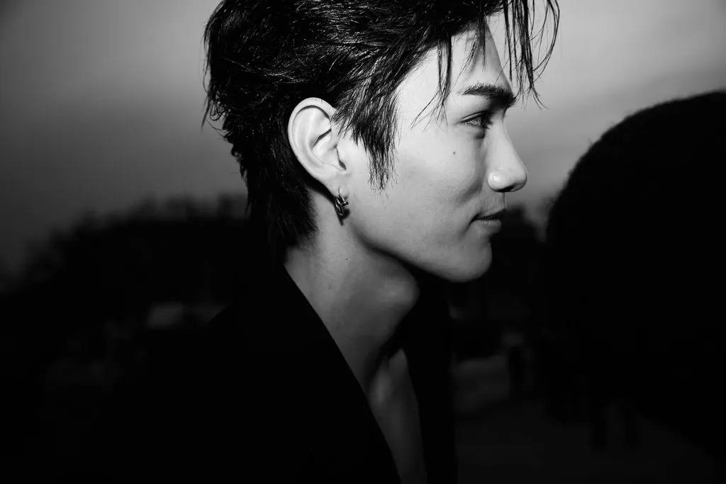 Black and white landscape portrait: a person with short tousled hair and a drop earring, in profile, against a dark background.