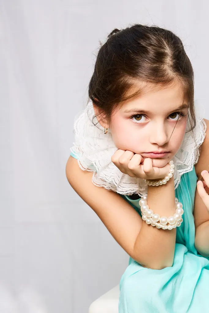 Colour portrait of a little girl with braided hair, chin in her hands, in a turquoise dress with a white lace collar.